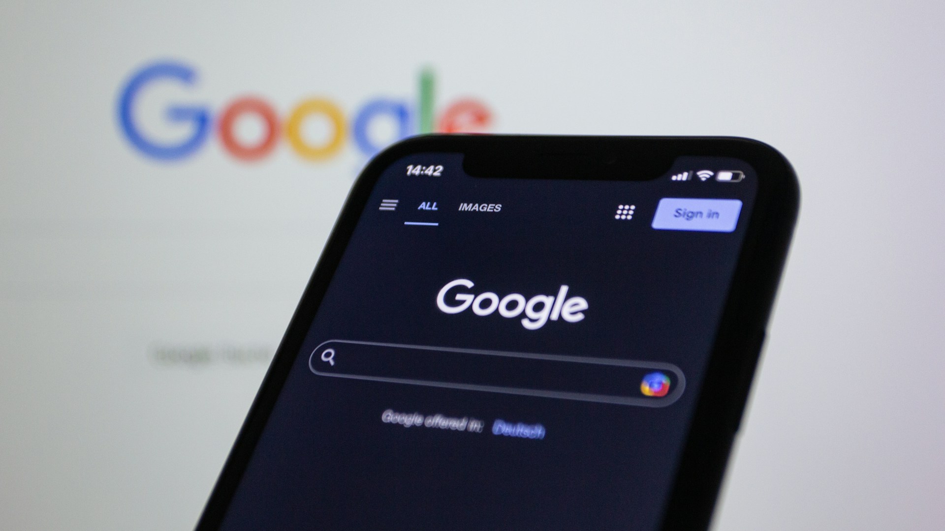 Google Search homepage displayed on a smartphone in dark mode with the Google logo blurred in the background