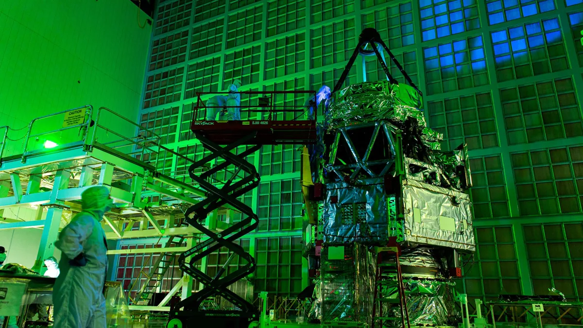 Engineers in cleanroom suits inspect the Roman Space Telescope under green laser light at NASA Goddard Space Flight Center