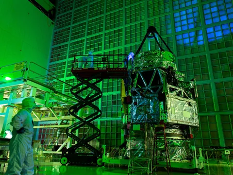 Engineers in cleanroom suits inspect the Roman Space Telescope under green laser light at NASA Goddard Space Flight Center