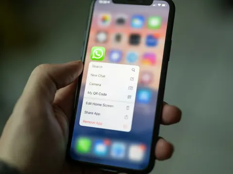 Hand holding an iPhone with WhatsApp app menu open on screen
