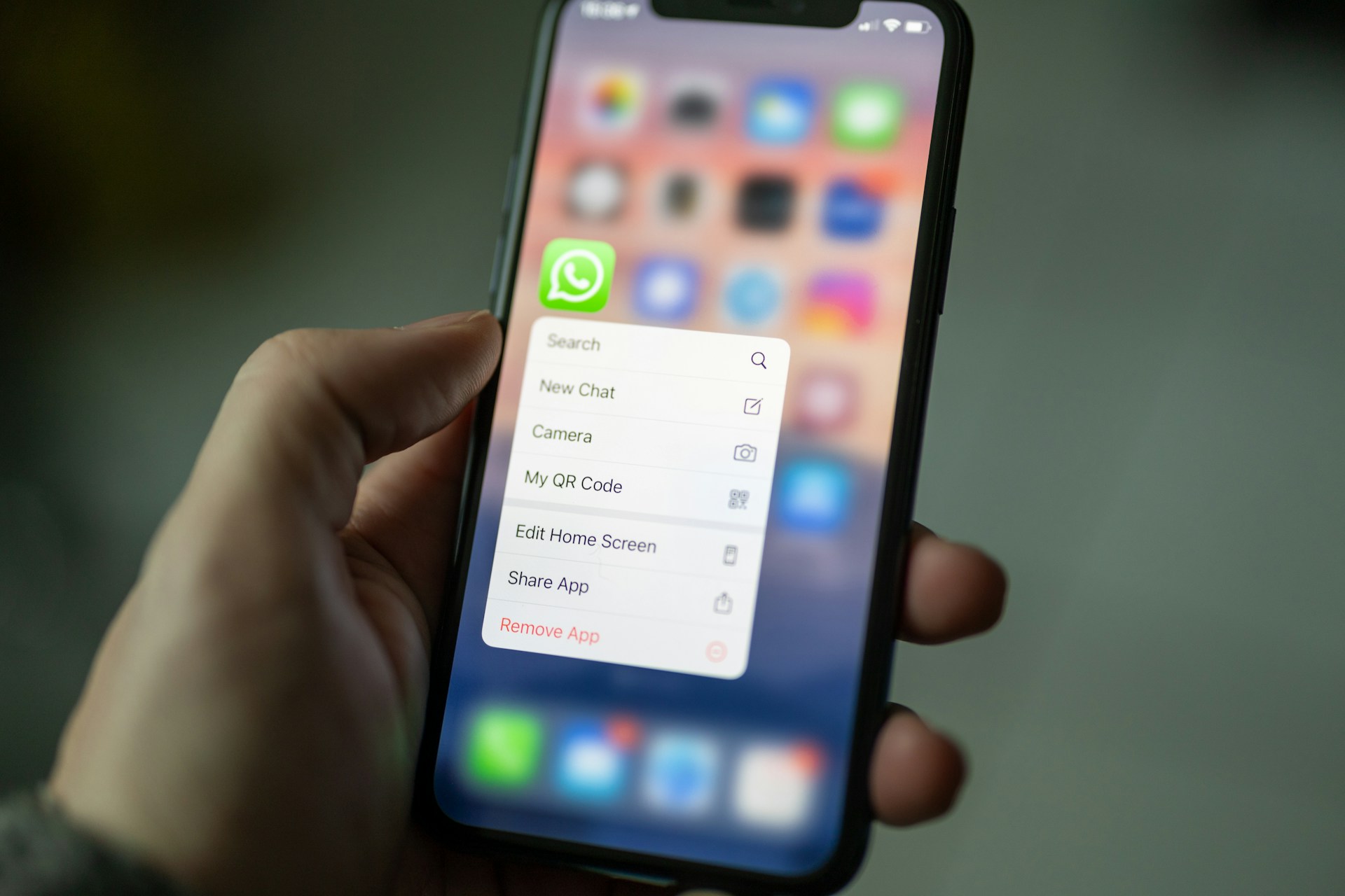 Hand holding an iPhone with WhatsApp app menu open on screen